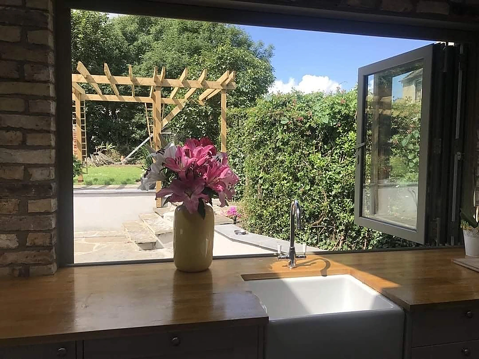 Aluminium bi-fold window above a kitchen sink, open to the garden