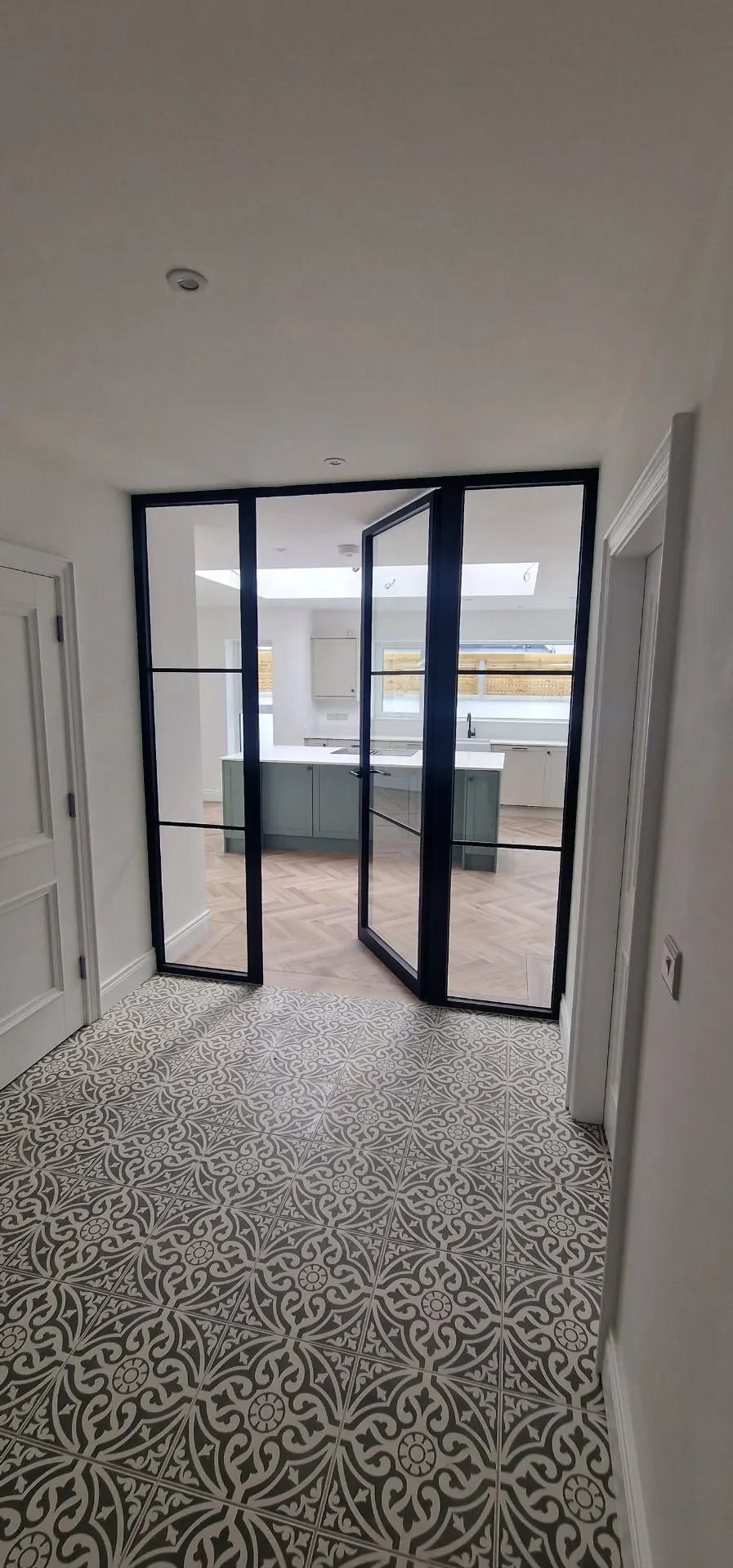Black steel-look glazed internal door and screen between a tiled hallway and kitchen, Northern Ireland
