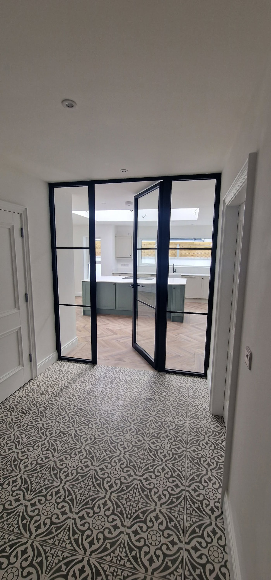 Black steel-look glazed internal door and screen between a tiled hallway and kitchen, Northern Ireland