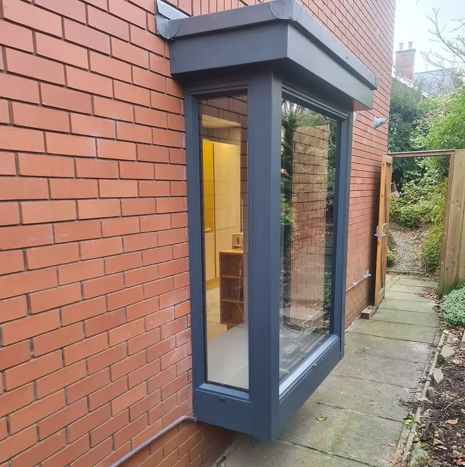 Aluminium box bay window projecting from a red brick wall